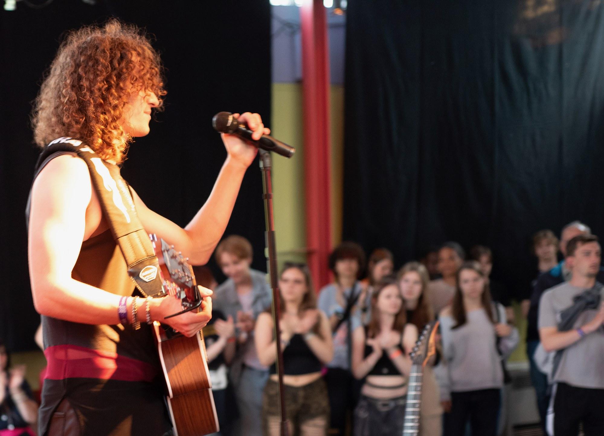 Gitarrist und Sänger mit lockigem Haar performt vor dem Publikum bei der klangrevier openstage