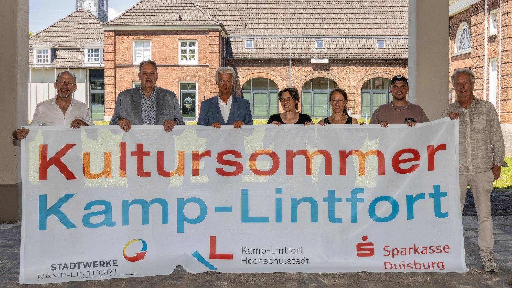 Sieben Personen halten ein großes Banner mit der Aufschrift Kultursommer Kamp-Lintfort vor dem Schirrhof, darauf die Logos von Stadtwerken und Sparkasse (Foto: Rainer Hoheisel / FUNKE Foto Services)