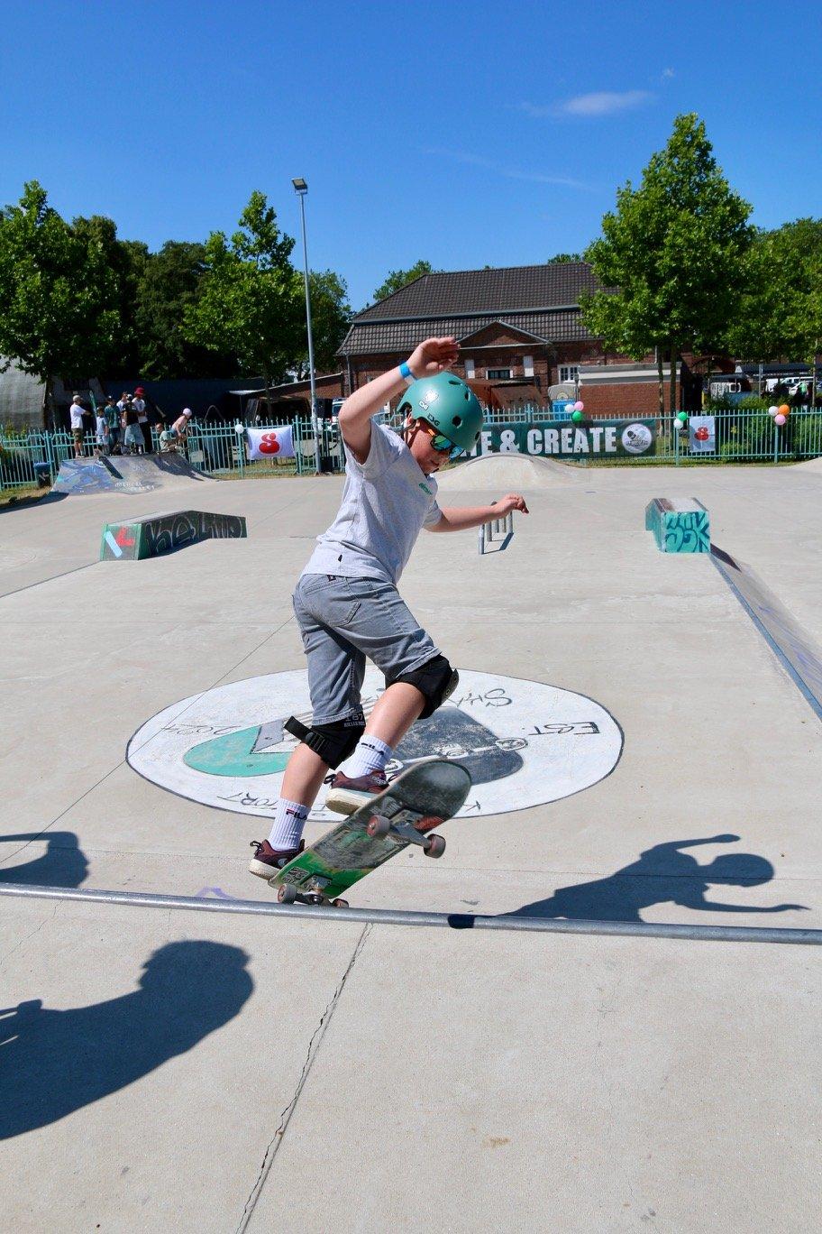 Junge mit türkisem Helm fährt Skateboard im Skatepark am Schirrhof