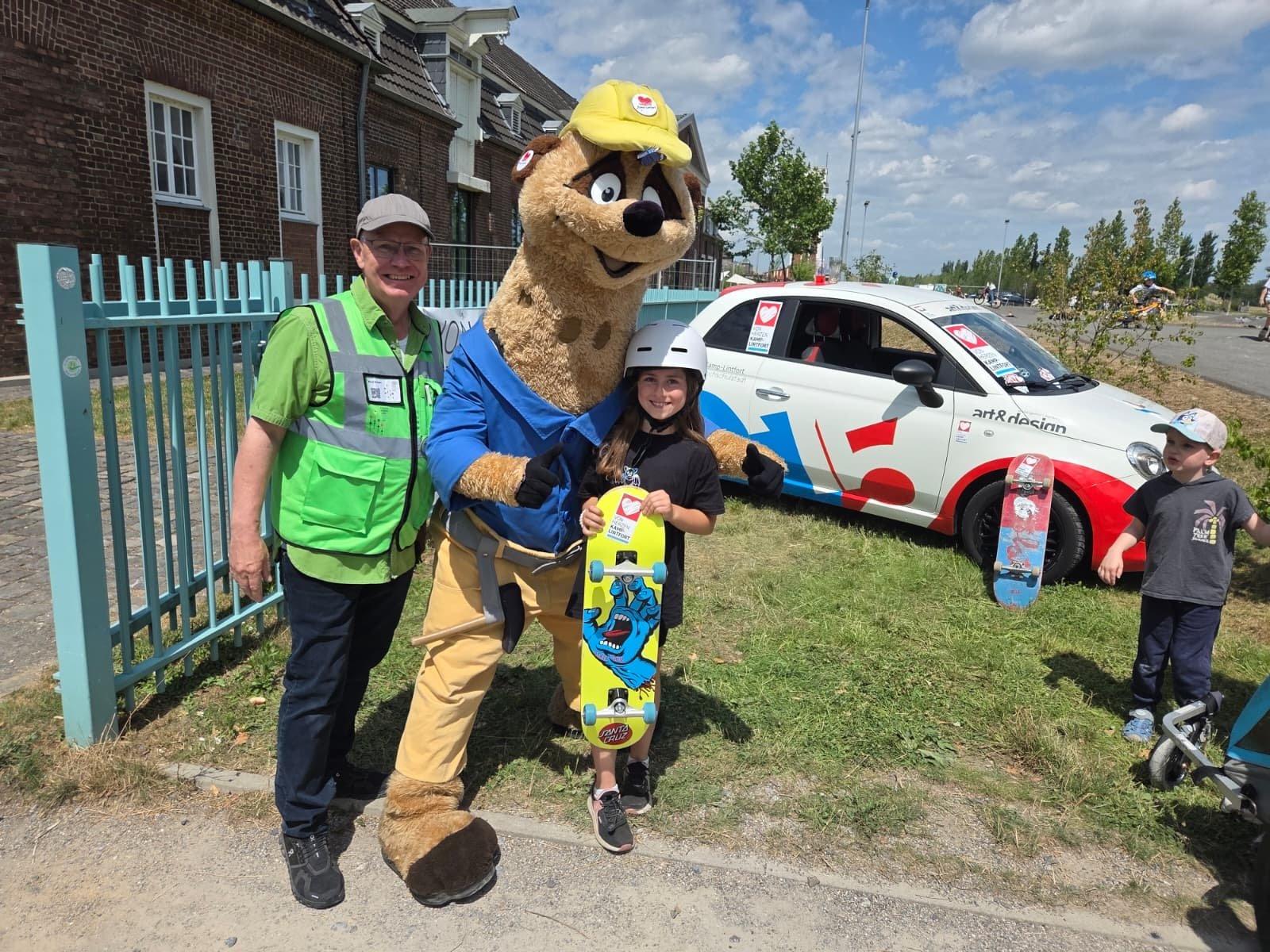 Maskottchen Kalli mit einem Mädchen und Skateboard neben dem Von-Herzen-Auto
