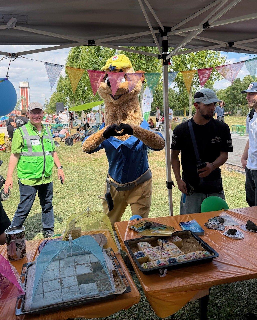 Maskottchen Kalli formt ein Herz am Kuchenstand beim Kultursommer
