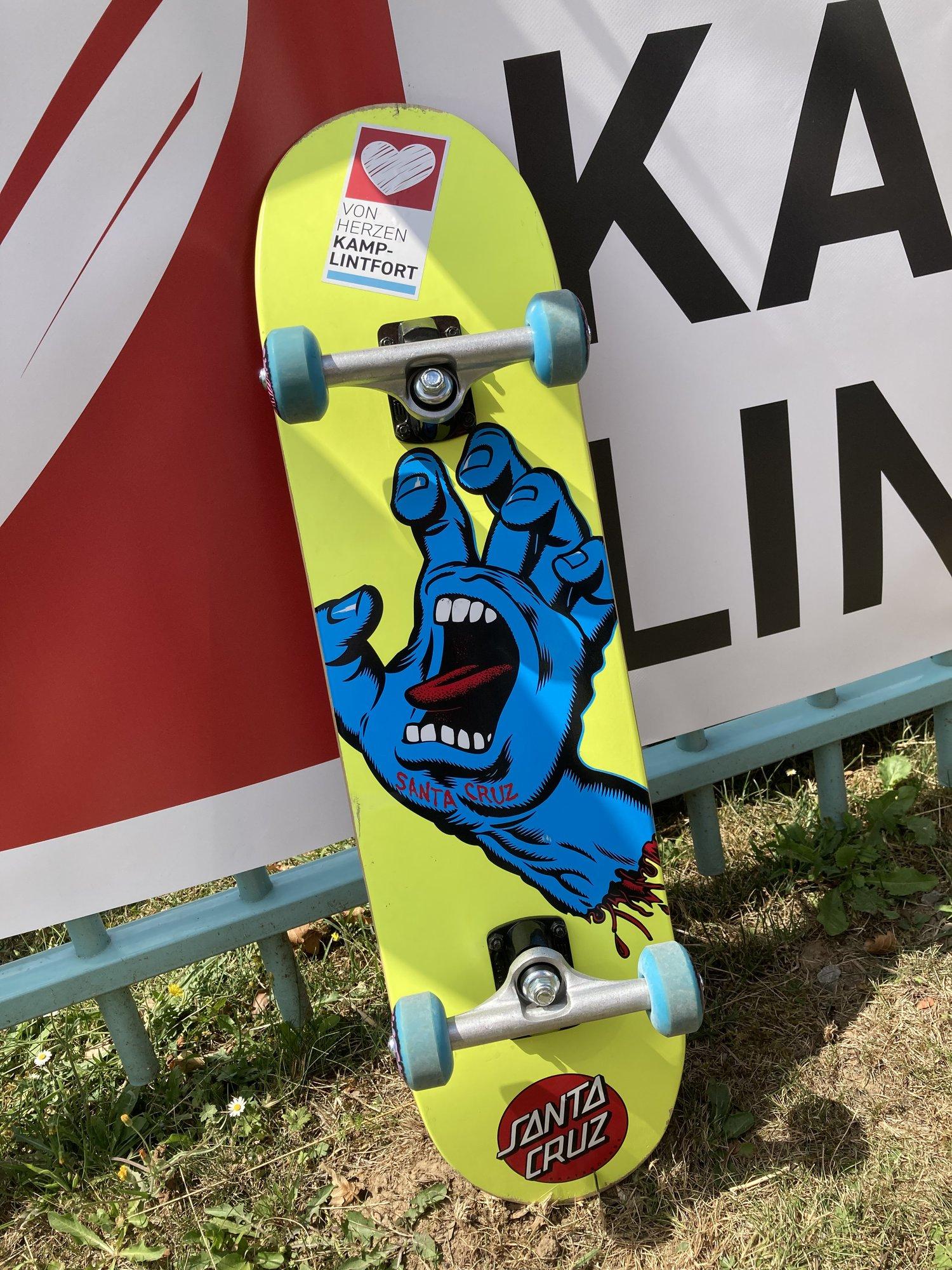 Santa-Cruz-Skateboard mit Von-Herzen-Kamp-Lintfort-Aufkleber am Banner