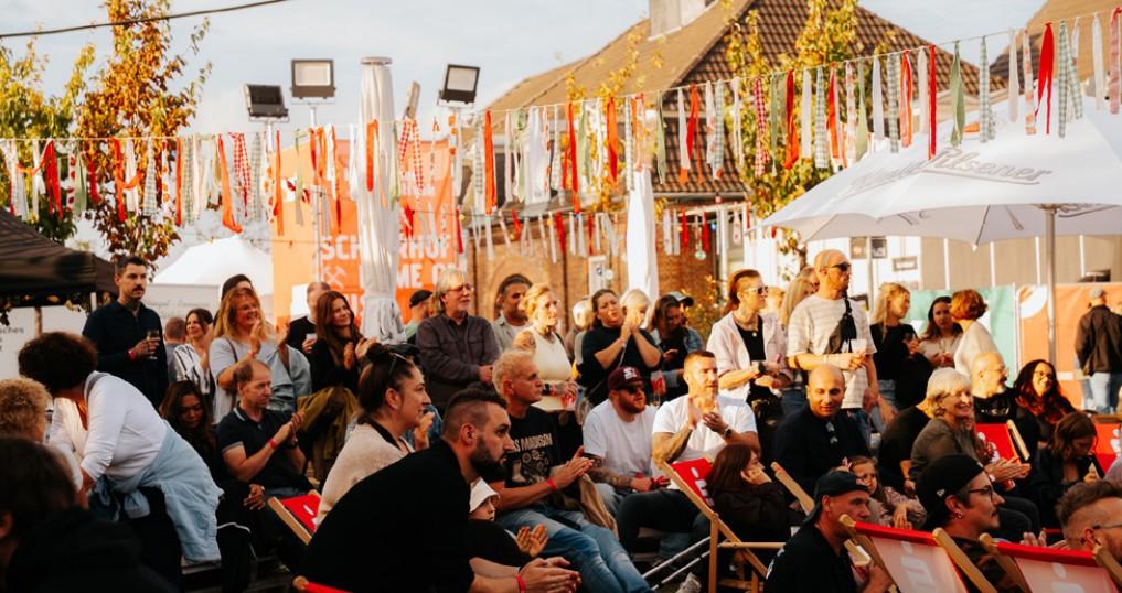 Applaudierendes Publikum im Lounge- und Biergartenbereich unter bunten Wimpelketten und Sonnenschirmen