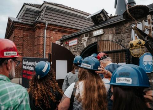 Besucherinnen und Besucher mit Schutzhelmen bei einer Führung vor dem historischen Ziegelgebäude des Schirrhofs