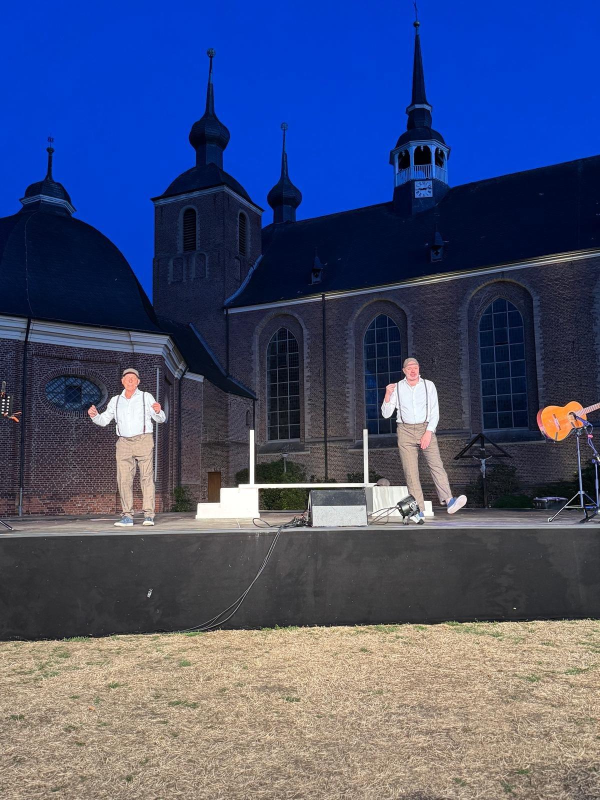 Zwei Darsteller auf der beleuchteten Bühne vor der Kulisse des Klosters Kamp zur blauen Stunde