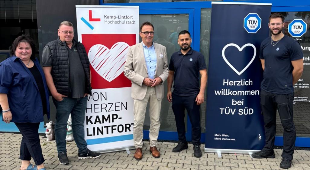 Gruppenfoto vor dem TÜV SÜD Auto Partner Prüfzentrum Niederrhein in Kamp-Lintfort mit Roll-ups von Von Herzen Kamp-Lintfort und TÜV SÜD