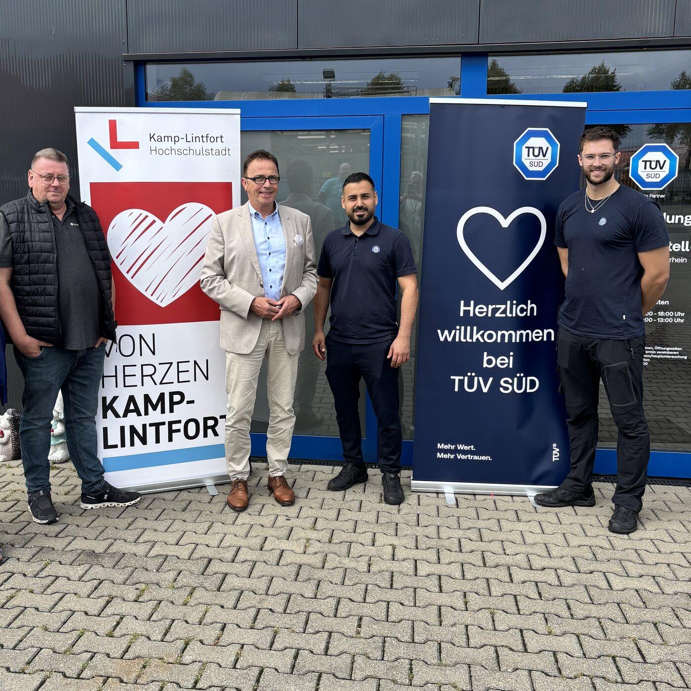 Gruppenfoto vor dem TÜV SÜD Auto Partner Prüfzentrum Niederrhein in Kamp-Lintfort mit Roll-ups von Von Herzen Kamp-Lintfort und TÜV SÜD