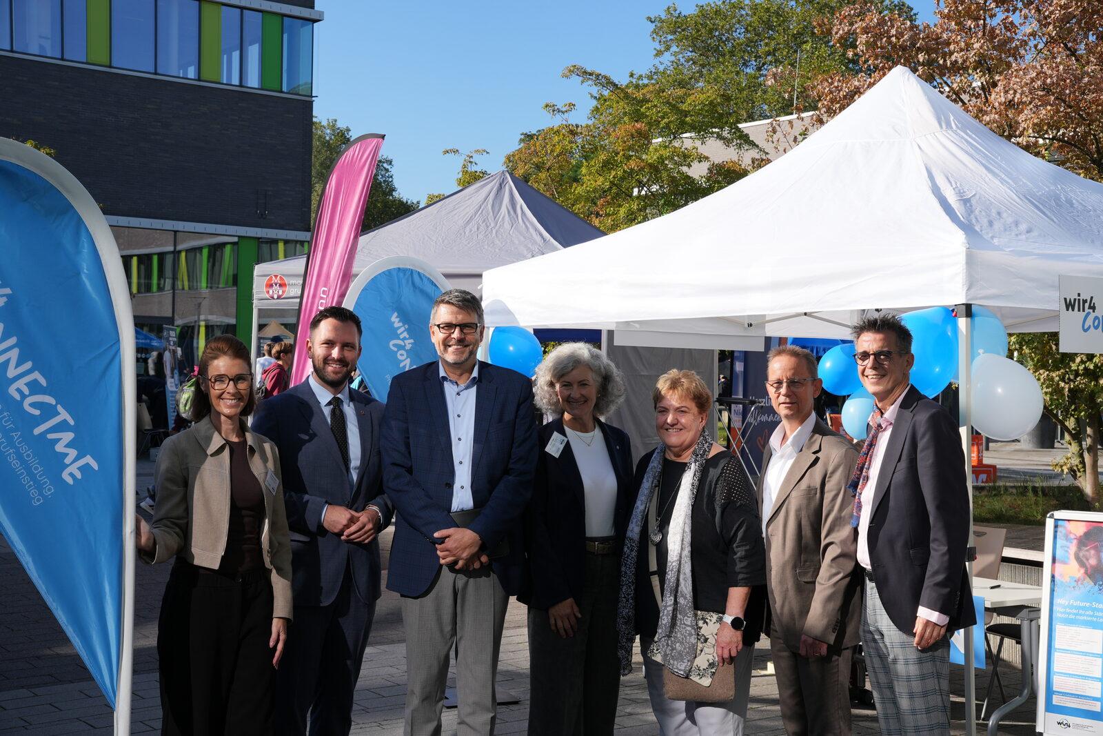 Gruppenfoto der Veranstalterinnen und Veranstalter der wir4connectMe 2026 vor den Beachflags und Messezelten auf dem Campus der Hochschule Rhein-Waal